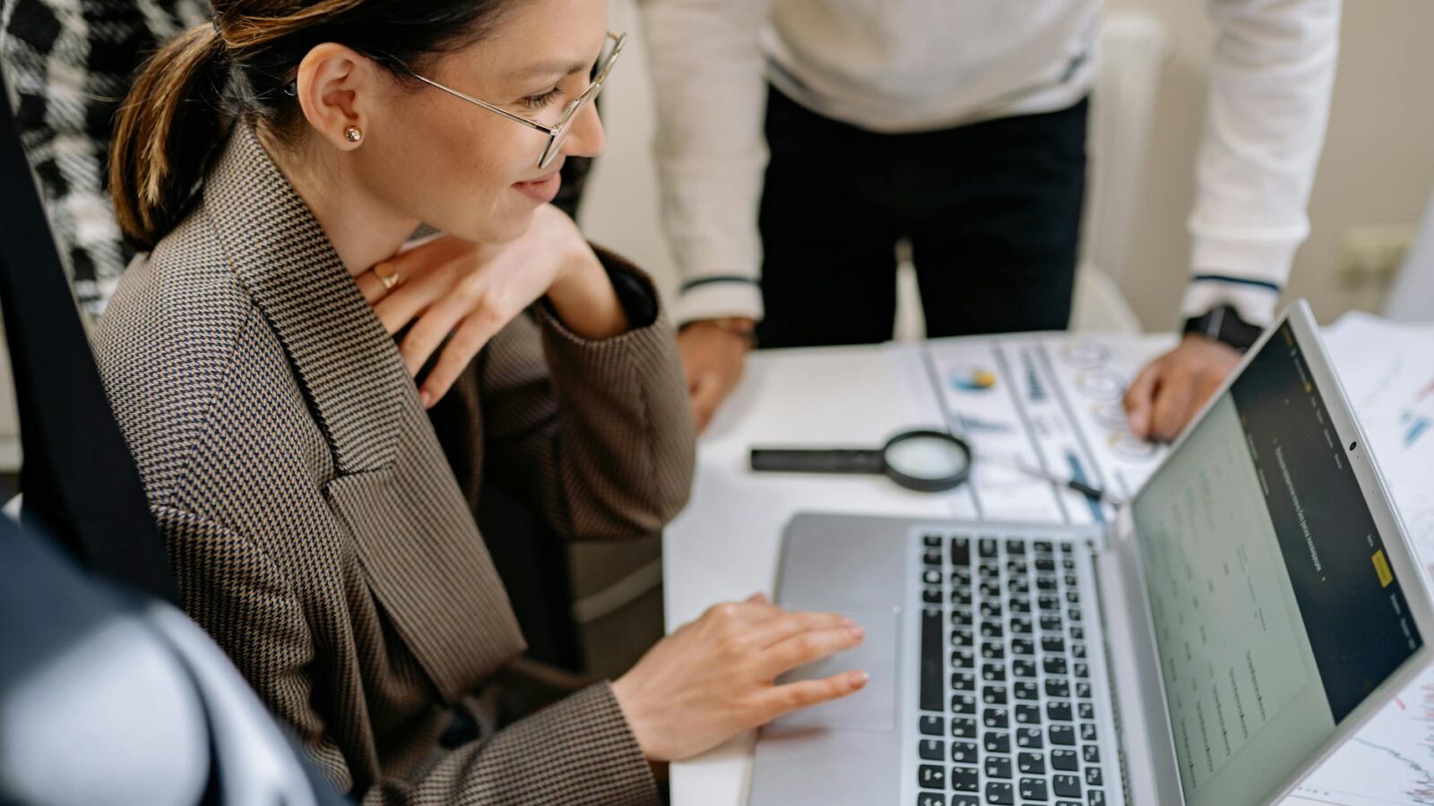 Businesswoman using laptop at office desk surrounded by colleagues, collaborating on project.