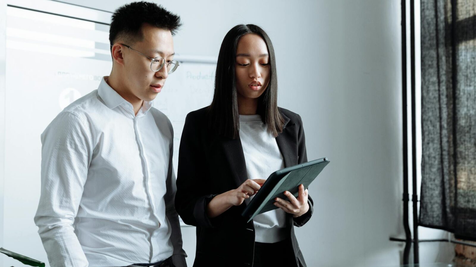 Two business people discussing work on a tablet in a modern office setting.