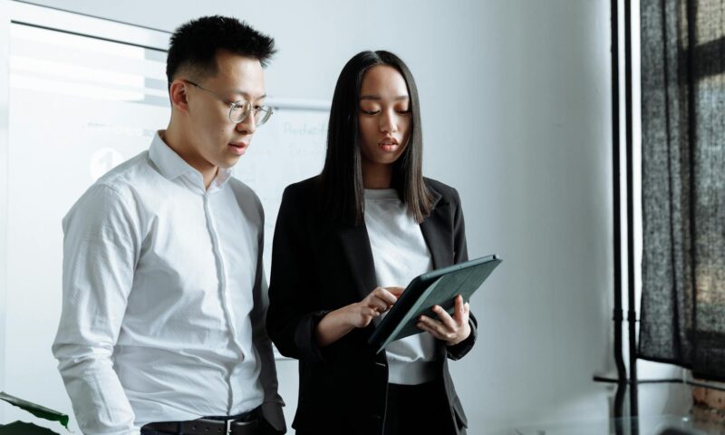 Two business people discussing work on a tablet in a modern office setting.